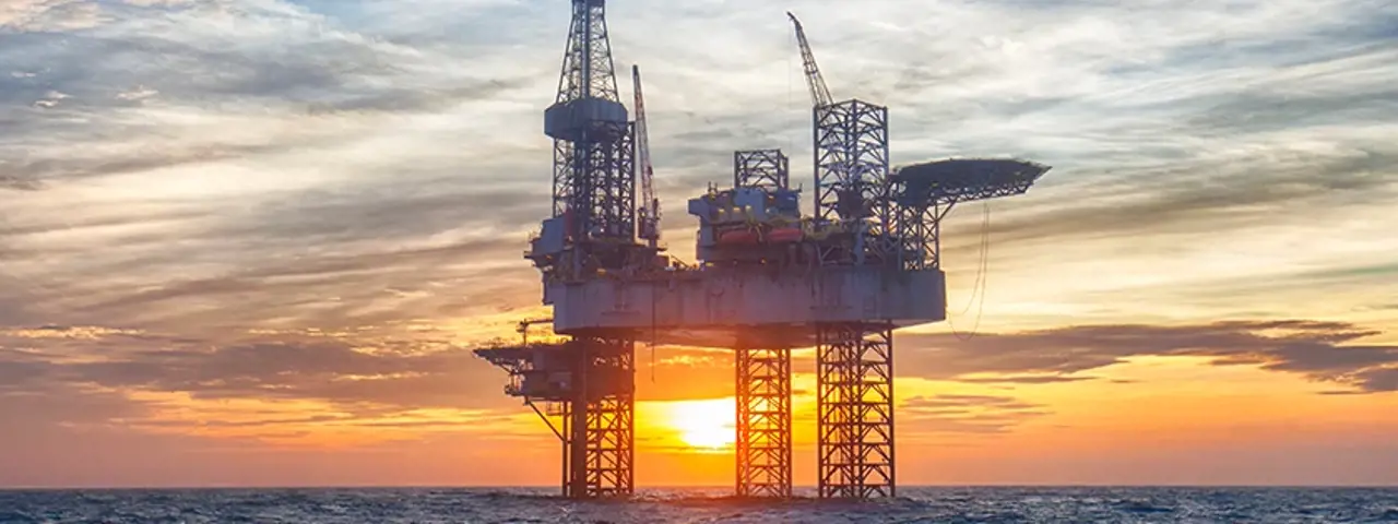 Offshore oil platform in ocean with sunset in background