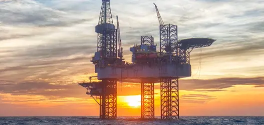 Offshore oil platform in ocean with sunset in background